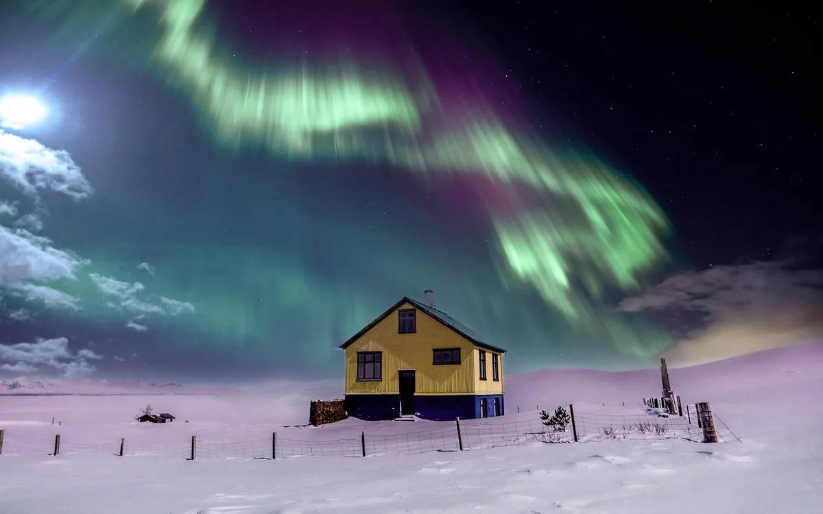 A green aurora over a lone house in the snow