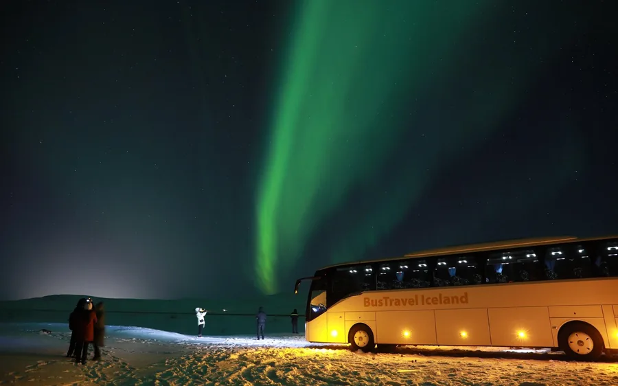 A coach parked under a green aurora on an Icelandic road