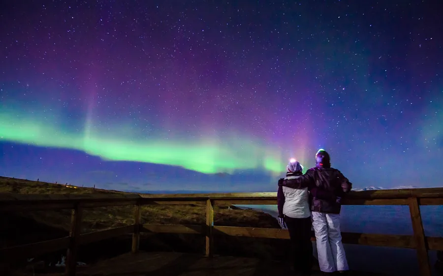 People watching a bright aurora from a viewpoint railing
